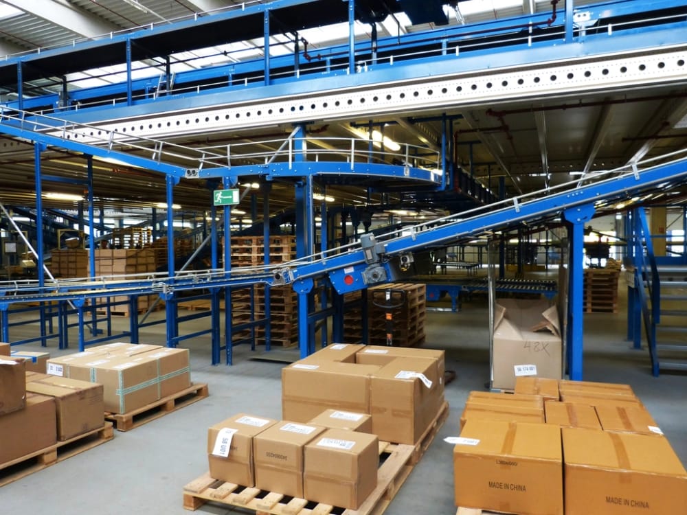 Returned cartons staged on pallets beside a conveyor in a receiving area, with one box opened for triage.
